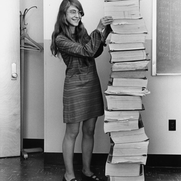 Margaret Hamilton standing beside a tall stack of printed Apollo flight-software listings at MIT in 1969.