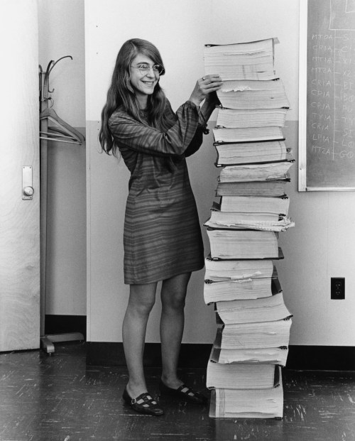 Margaret Hamilton standing beside a tall stack of printed Apollo flight-software listings at MIT in 1969.